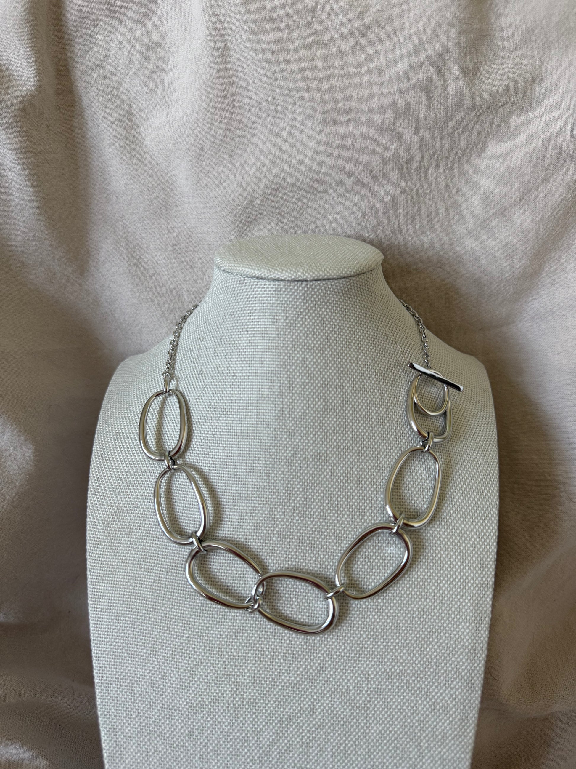 Silver necklace on a white mannequin bust against a beige fabric background