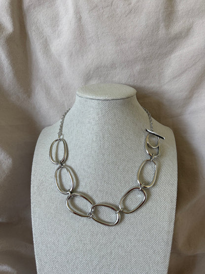 Silver necklace on a white mannequin bust against a beige fabric background