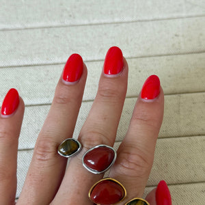 Hand wearing three rings with red gemstones on a light background