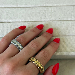 Hand with red nail polish wearing two rings on a light background