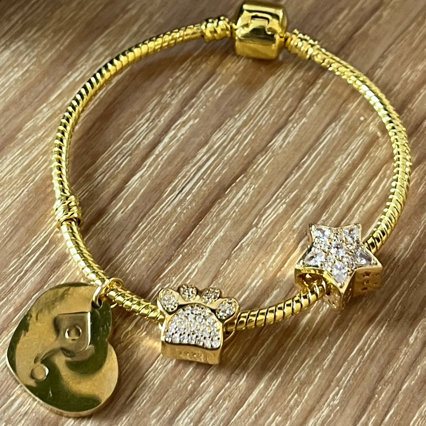 Gold bracelet with charms on a wooden surface next to a candle and mug.
