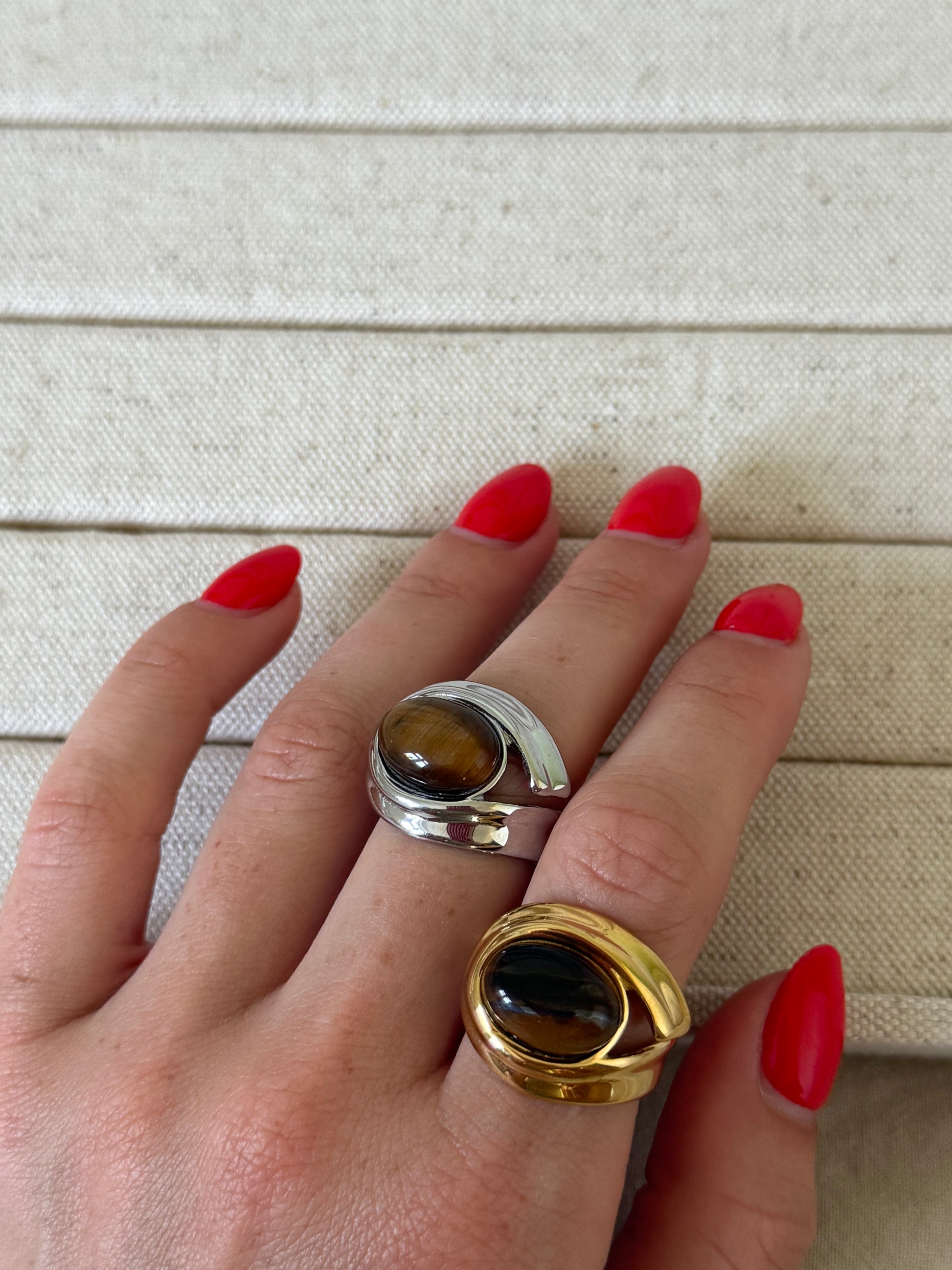 Hand wearing two rings with tiger's eye stones on a neutral background