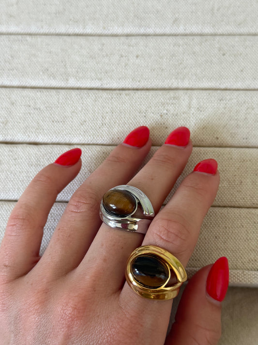 Hand wearing two rings with tiger's eye stones on a neutral background