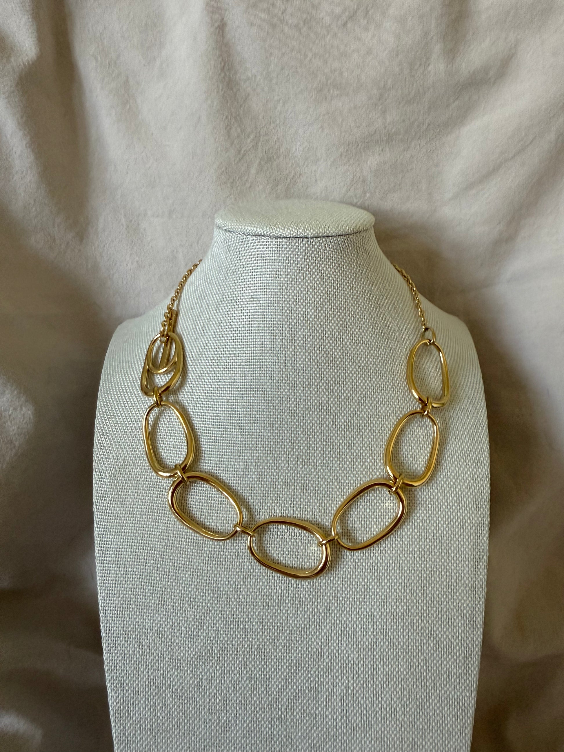 Gold chain necklace on a mannequin bust against a beige fabric background