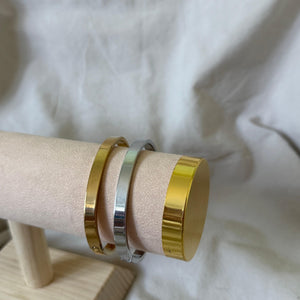 Two gold and silver bangles on a wooden stand with a white fabric background