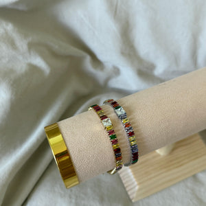 Multicolored beaded bracelet on a wrist with a gold ring, against a white fabric background