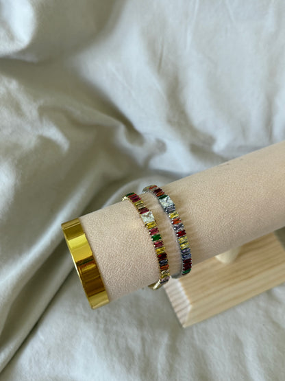 Multicolored beaded bracelet on a wrist with a gold ring, against a white fabric background