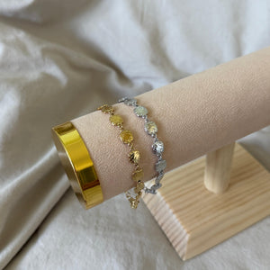 GOLD SILVER bracelets on a wooden stand against a white fabric background