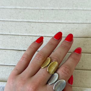 Hand wearing three shell-shaped rings on a beige fabric background