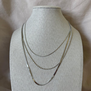 Three thin gold necklaces on a gray mannequin bust against a light background