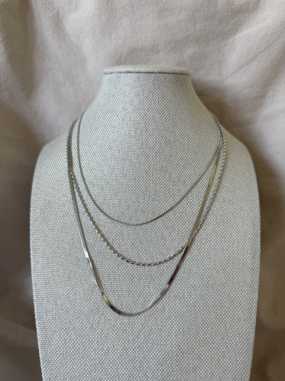 Three thin gold necklaces on a gray mannequin bust against a light background