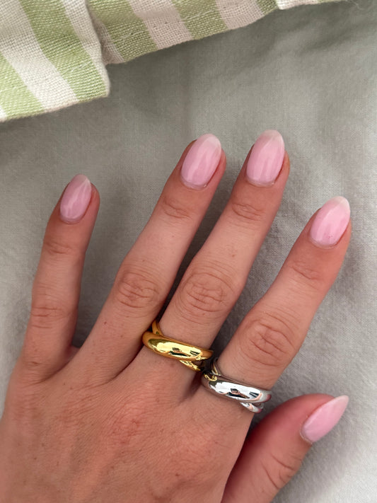 Hand wearing two rings with pink nail polish on a neutral background