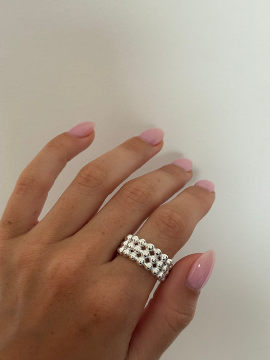 Hand wearing a silver ring with pink nail polish on a plain background