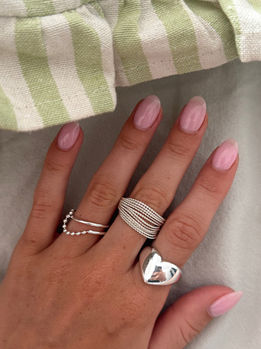 Hand with multiple silver rings on a neutral background
