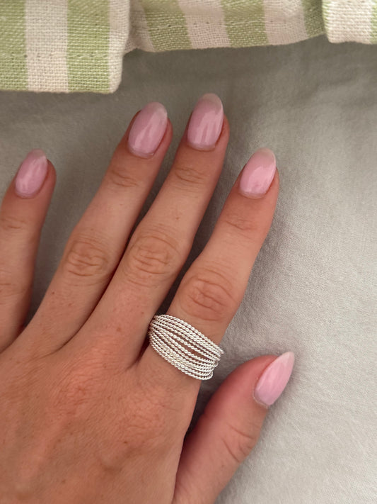 Hand wearing a silver ring with pink nail polish on a neutral background