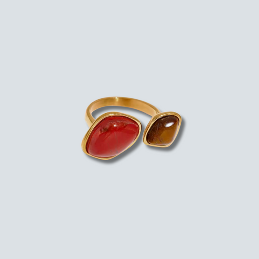 Gold ring with red and brown gemstones on a light gray background