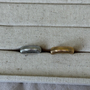 Two rings, one silver and one gold, on a textured surface.